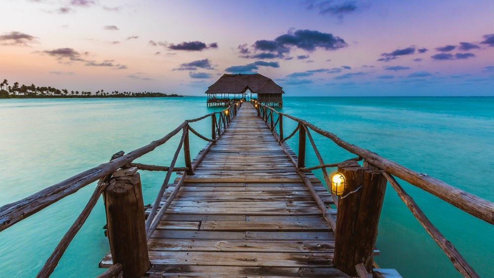 Wooden pier extending over turquoise water at sunset in East Africa.