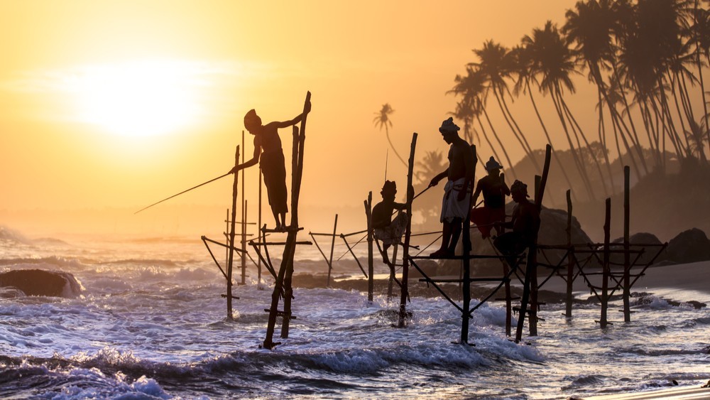 Stilt fishermen silhouetted at sunset along the coast of Sri Lanka.