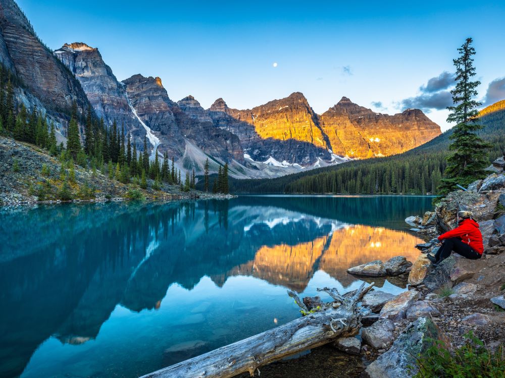 woman sitting along riverbed looking at mountains