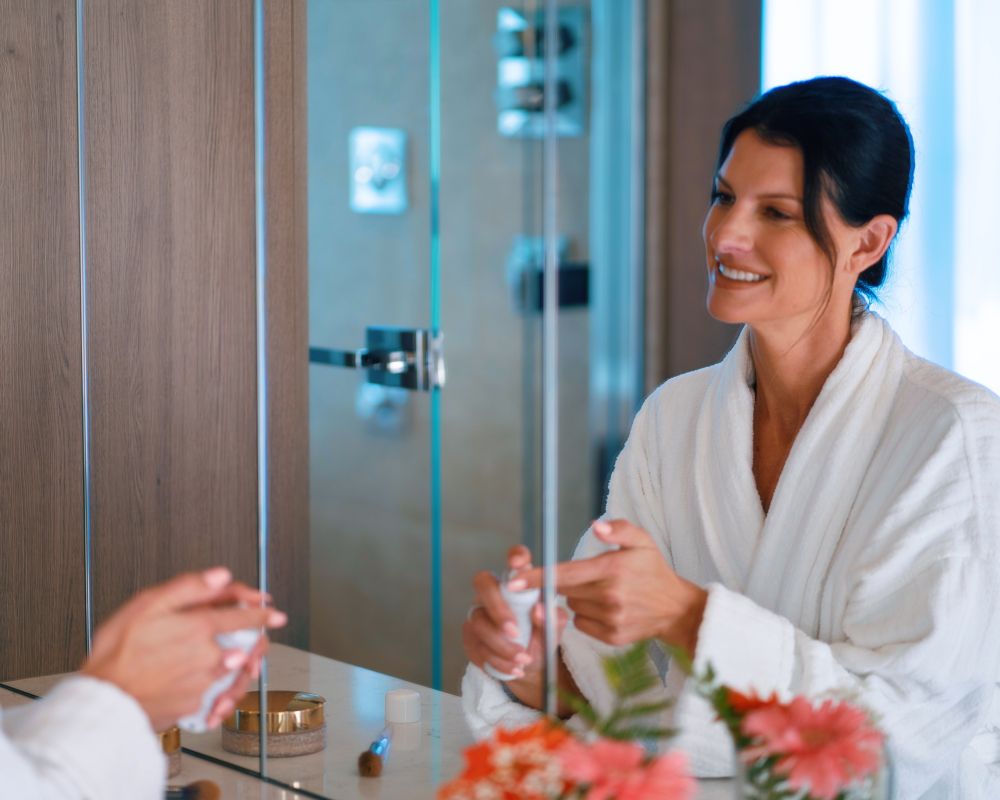 woman looking in mirror applying face product