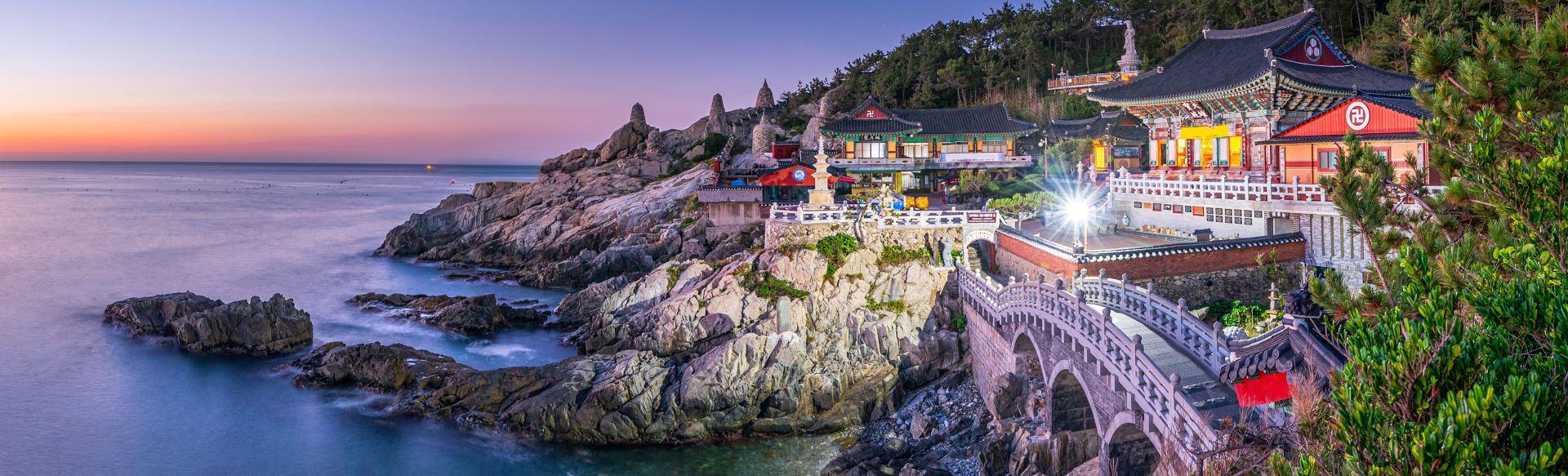 Coastal temple in Asia at sunrise, overlooking calm blue waters and rocky cliffs.