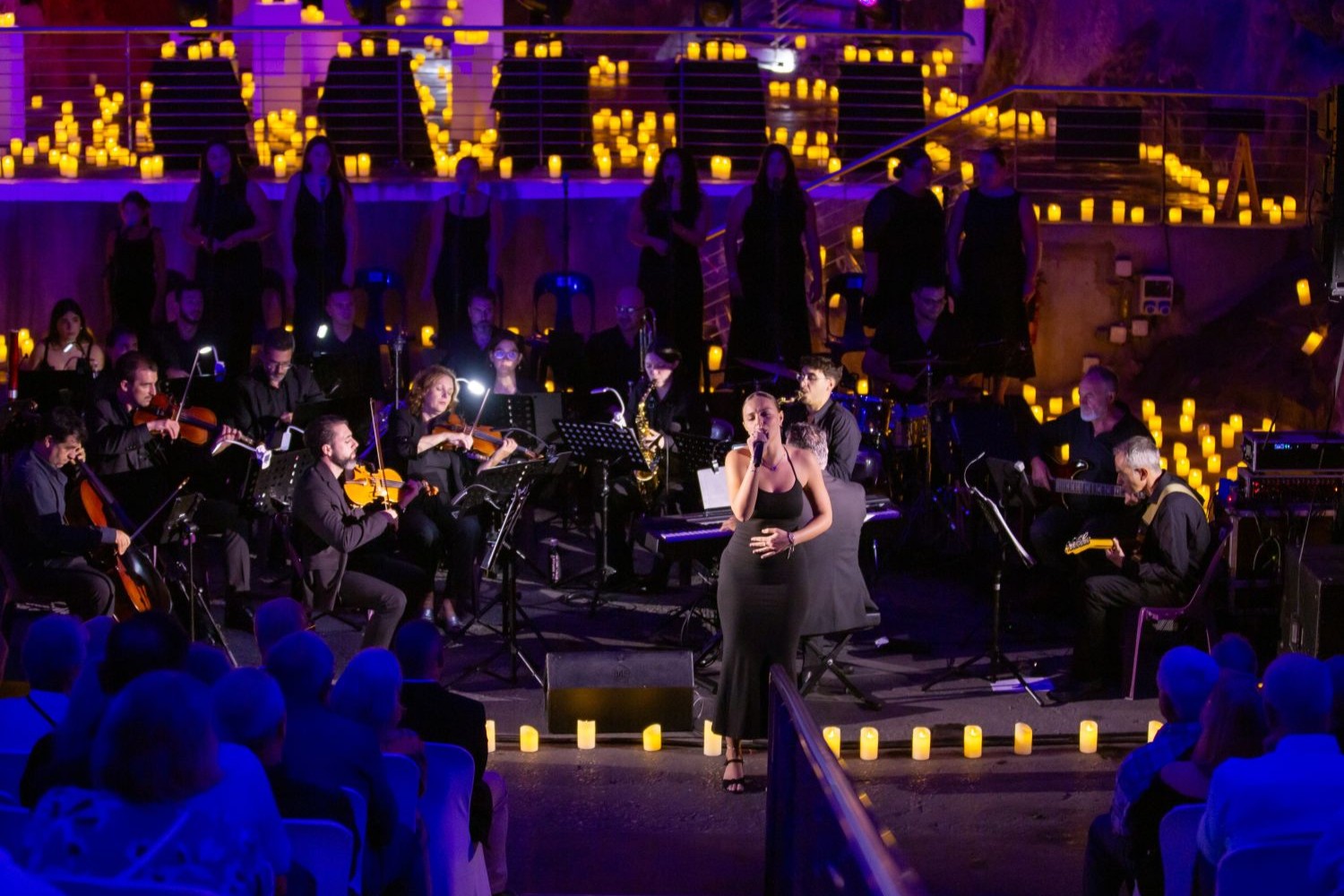 woman singing in candlelit space in front of an orchestra for an audience
