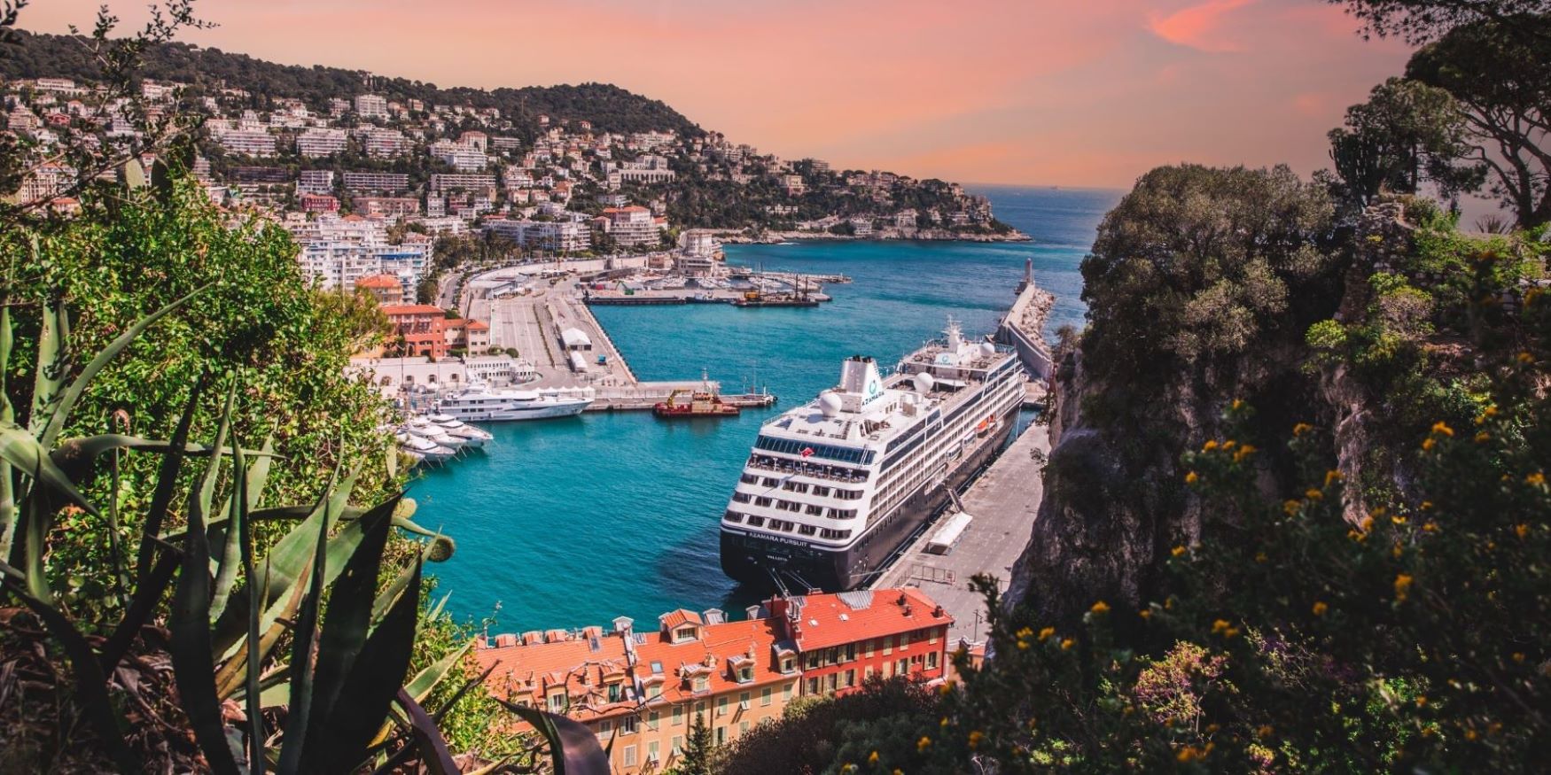 Cruise ship in the port of Nice, France, with colorful buildings and hillside backdrop.