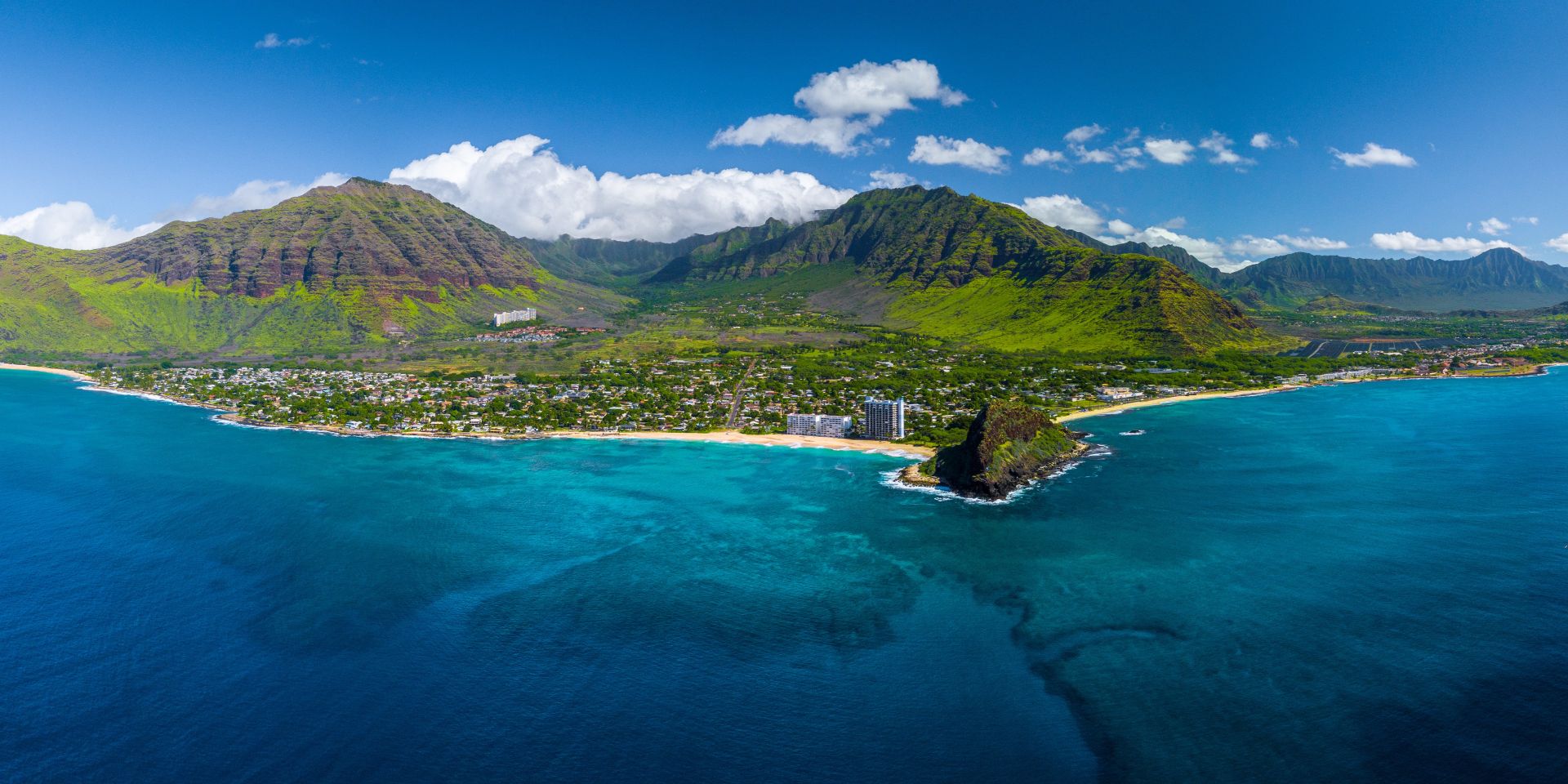 aerial view of Oahu, Hawaii's beach coastline in front of lush green mountains