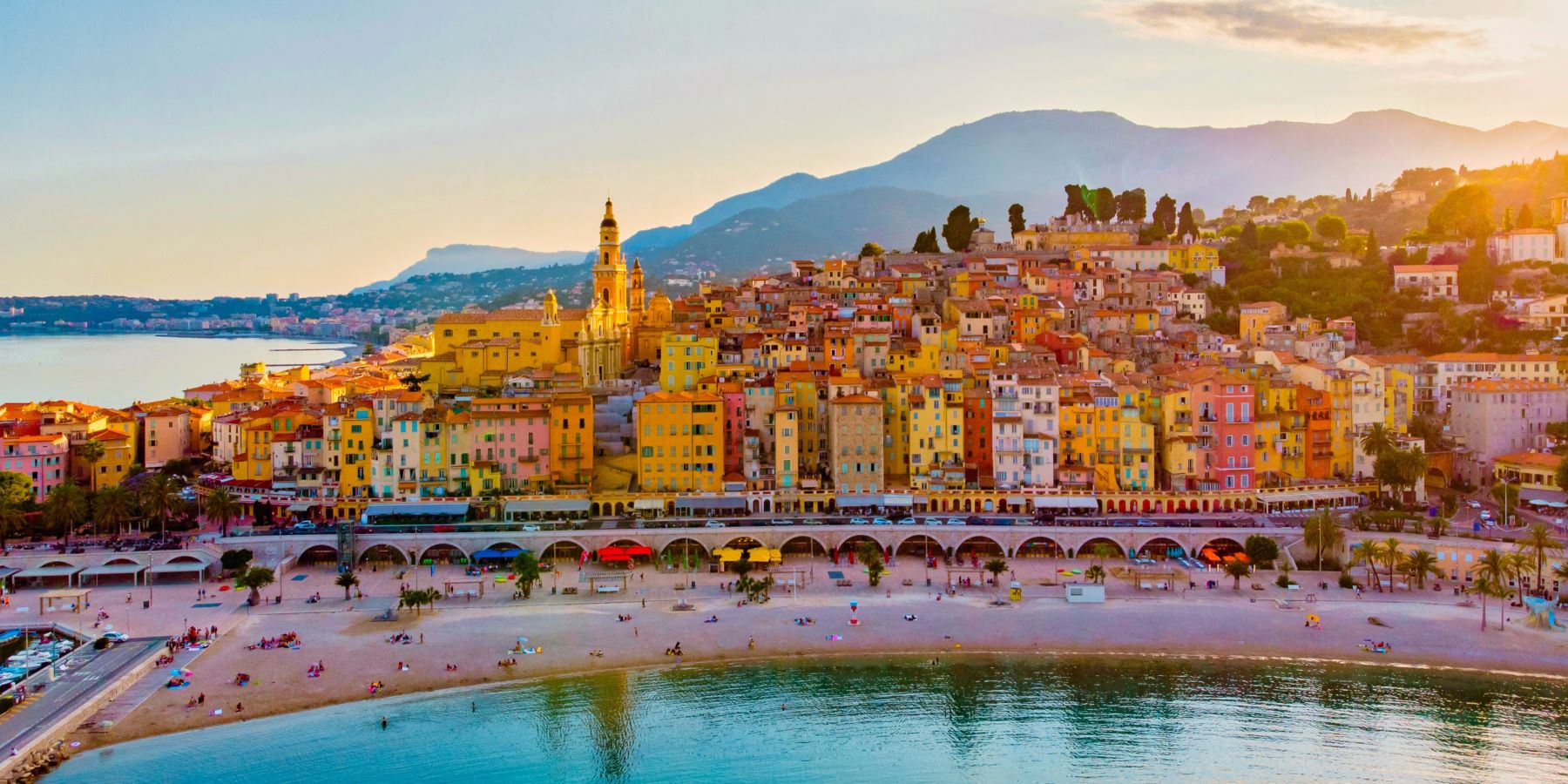 Late afternoon on a French beach in the foreground in front on a busy roadway framing a colorful coastal community of homes and shops.