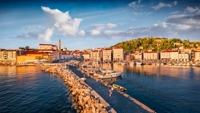 Piran waterfront at golden hour with sailboats and the town's hilltop walls