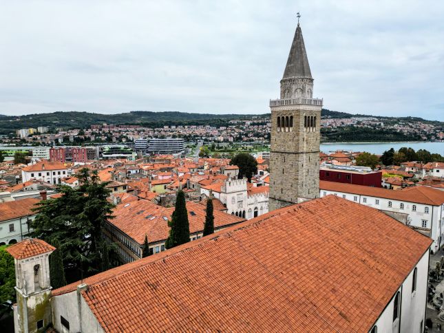 Aerial view over Koper's terracotta rooftops toward the Adriatic Sea from the bell tower