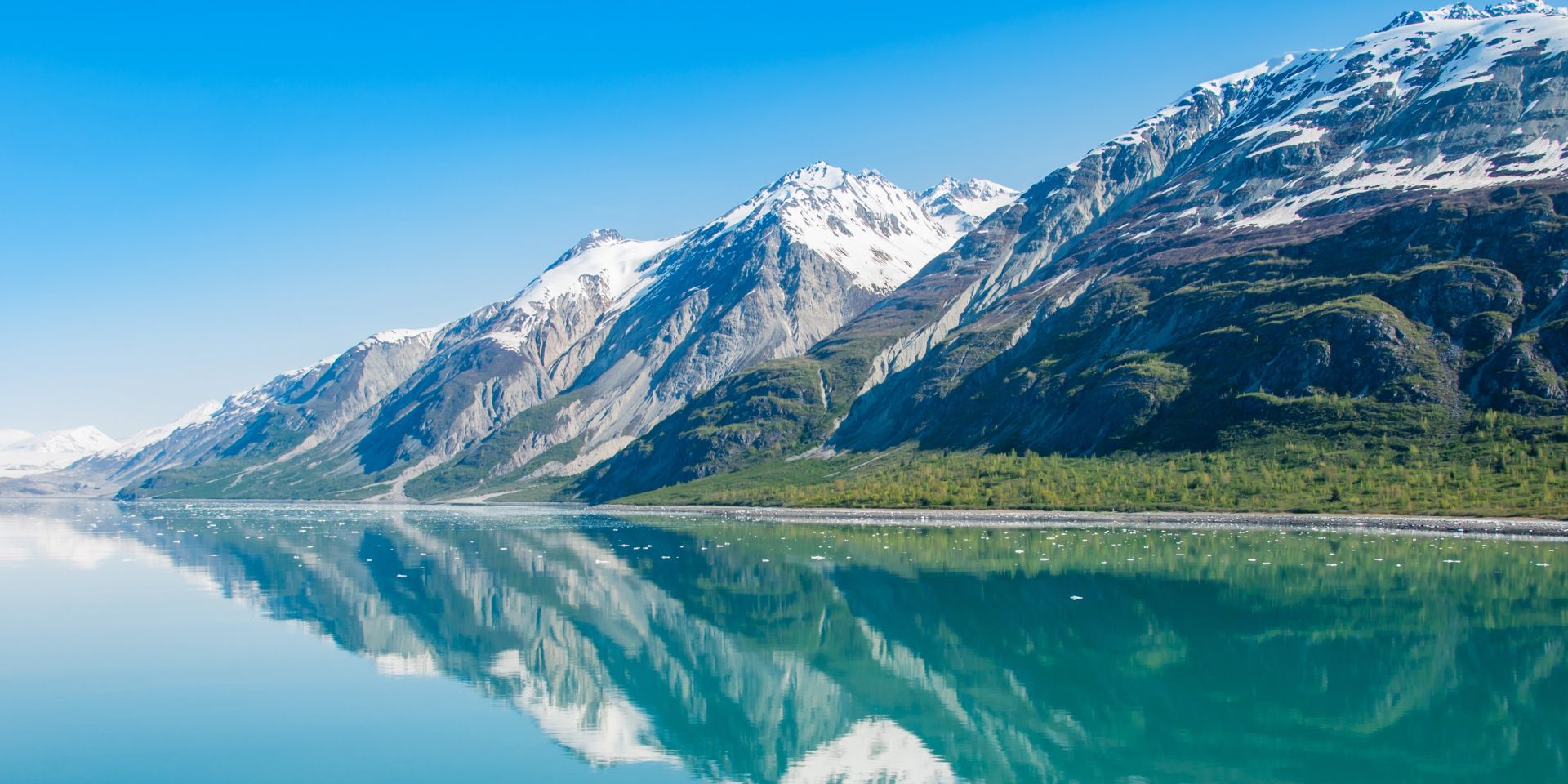 Snow-capped mountains reflected in calm turquoise waters along Alaska’s Inside Passage