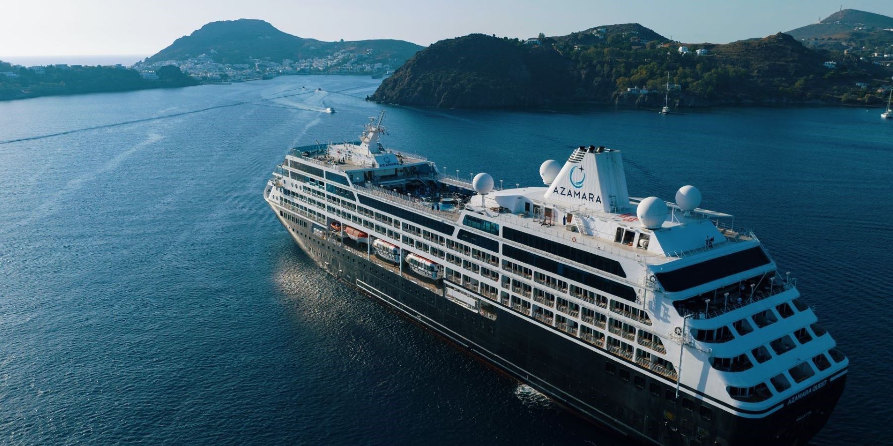 cruise ship sailing into port in calm water around hilly land formations