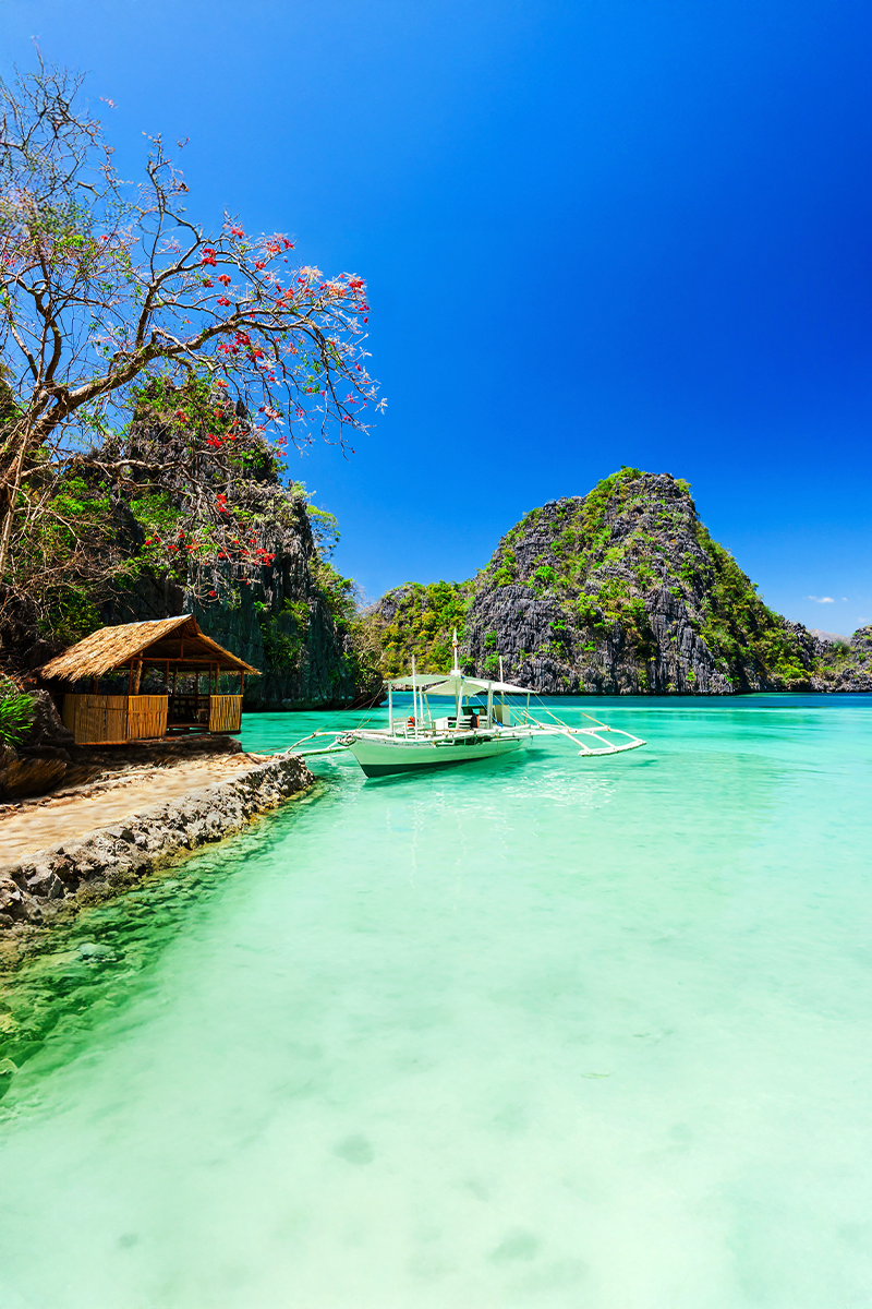 Clear turquoise waters and limestone cliffs with a traditional outrigger boat in Coron.