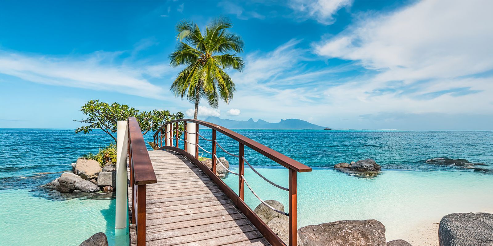 Papeete, French Polynesia lagoon with a wooden footbridge, palm tree, and turquoise water.