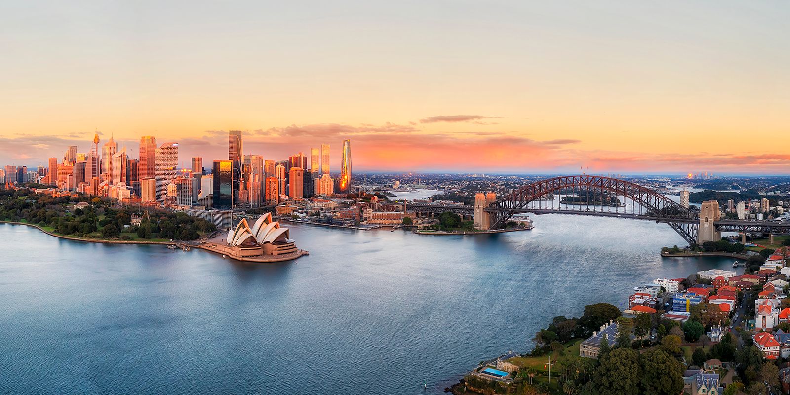 Sydney, Australia harbor at sunset with the Opera House, Harbour Bridge, and city skyline.
