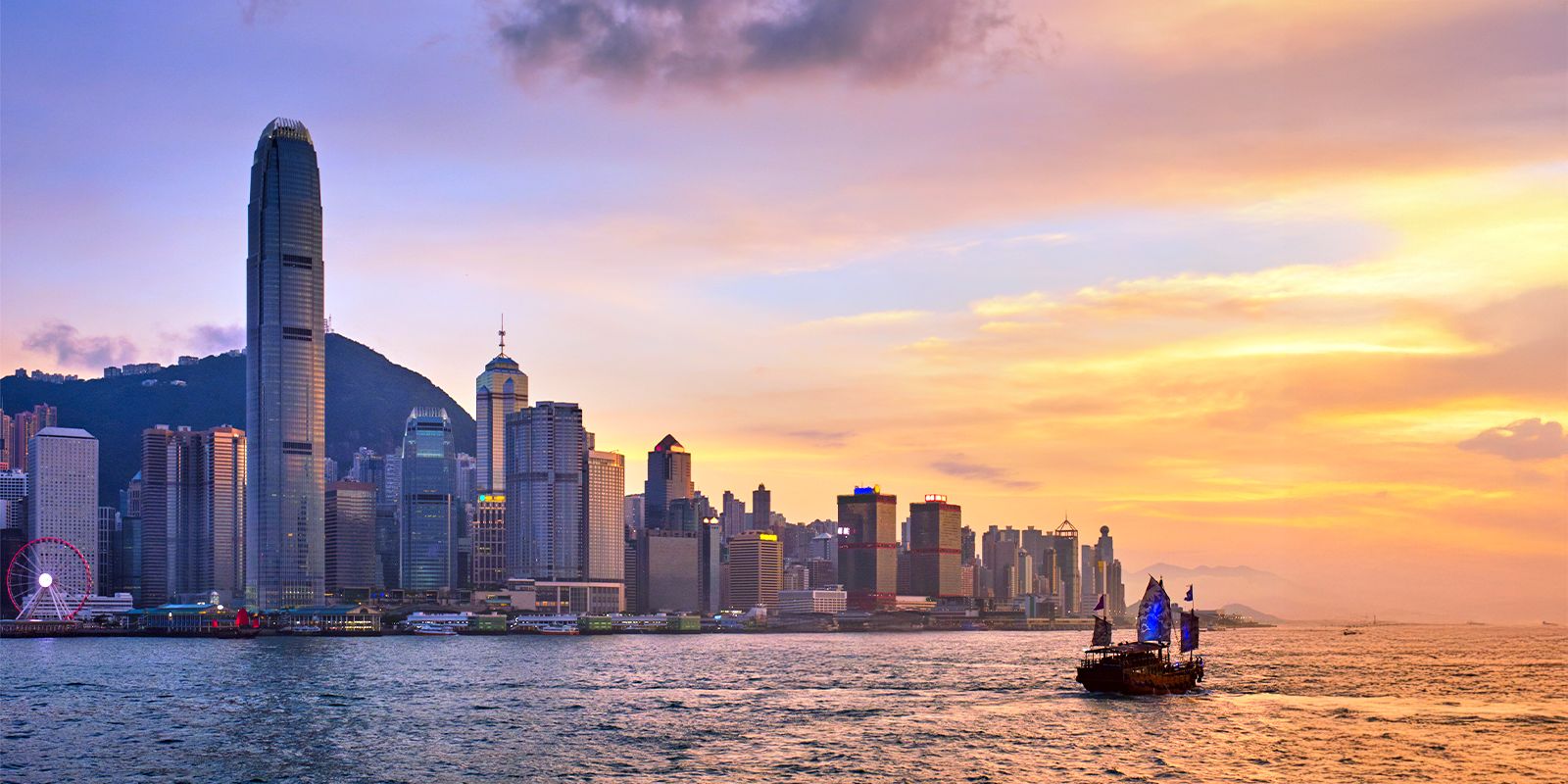 Hong Kong skyline at sunset with a traditional junk boat on Victoria Harbour.