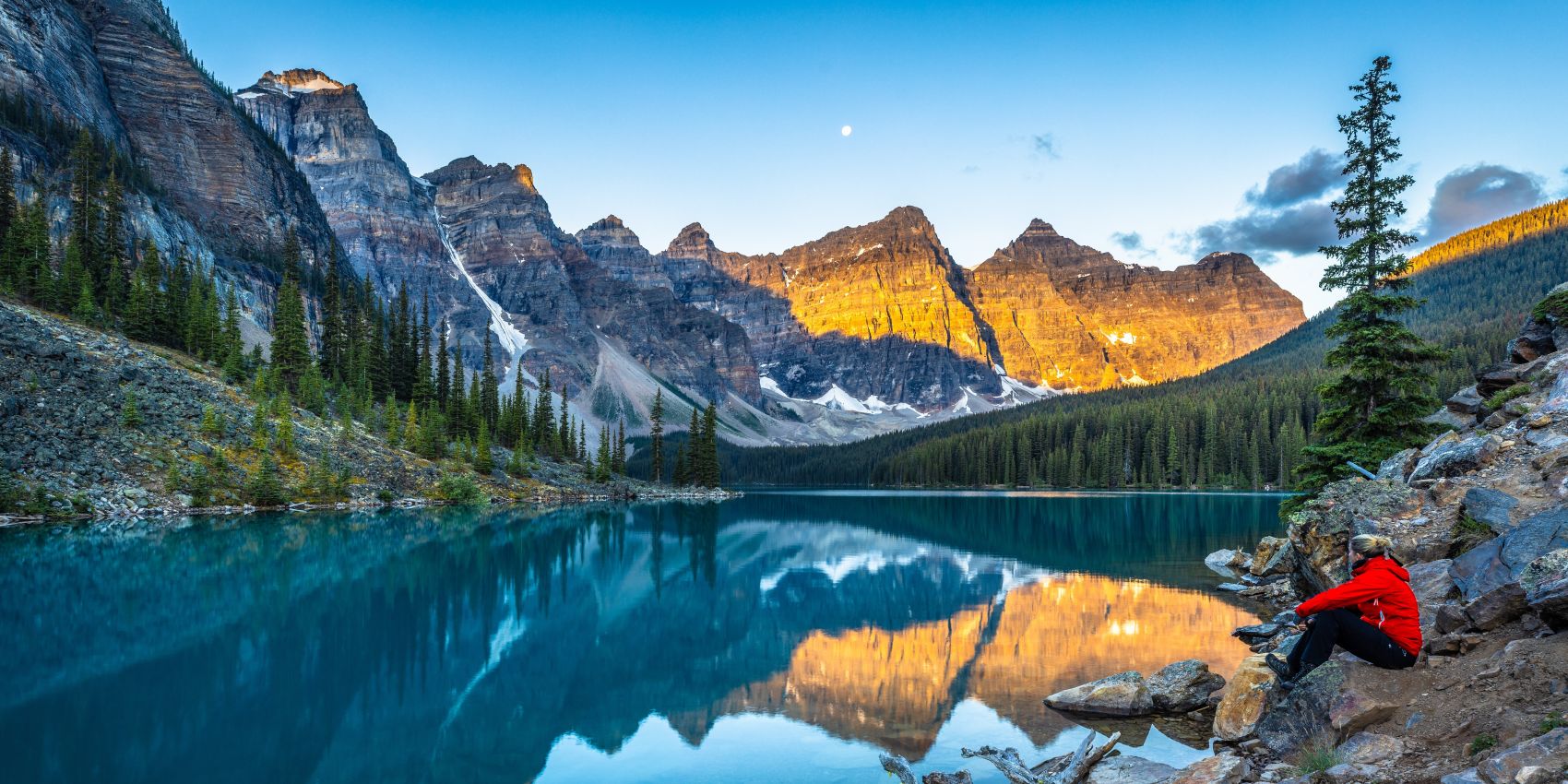 Traveler overlooking the turquoise waters and sunrise-lit peaks of Moraine Lake in Banff National Park, Canada.!''