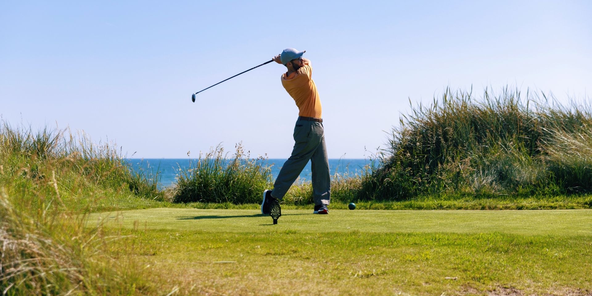 Golfer teeing off on a seaside links course with ocean views, representing Azamara's luxury golf cruises