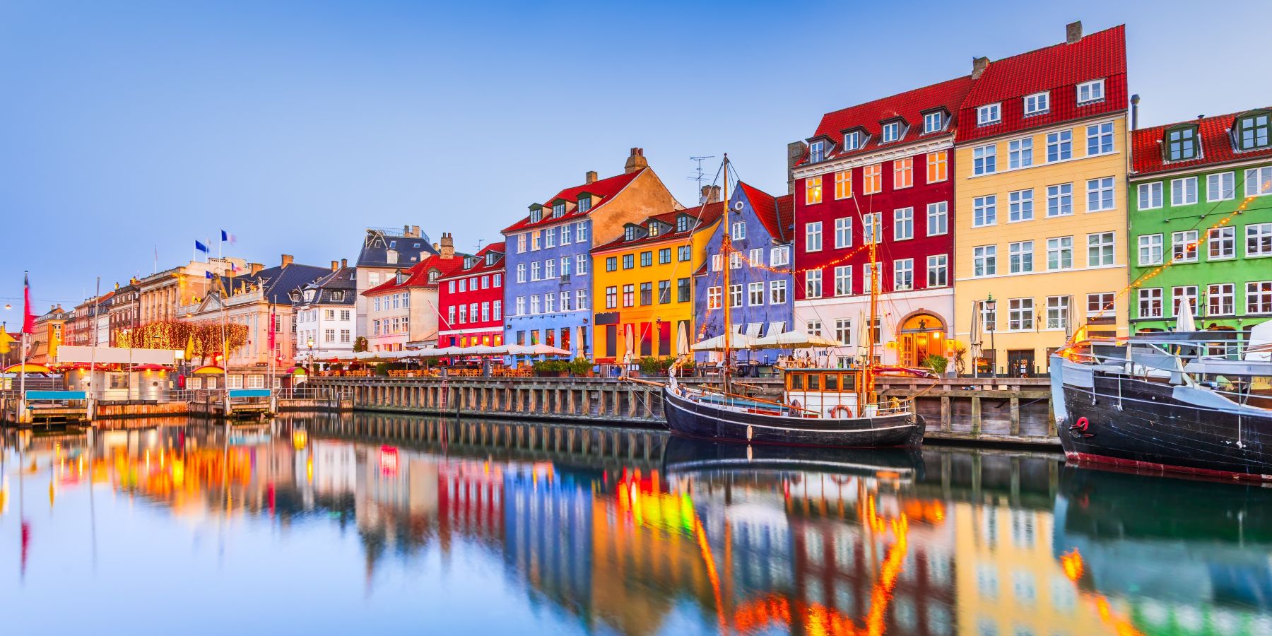 Colorful historic buildings lining Nyhavn harbor in Copenhagen, Denmark, with boats reflected in calm water at dusk.