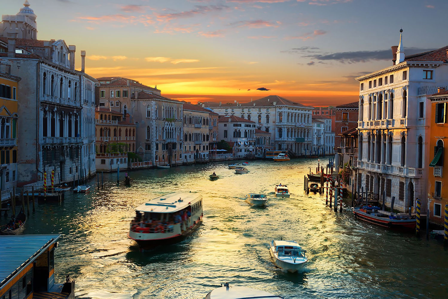 A vaporetto cruises a canal in Venice at sunset.