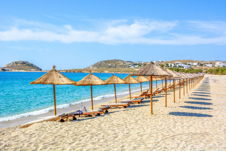 Sandy beach in Mykonos near the blue sea with sun beds and umbrella