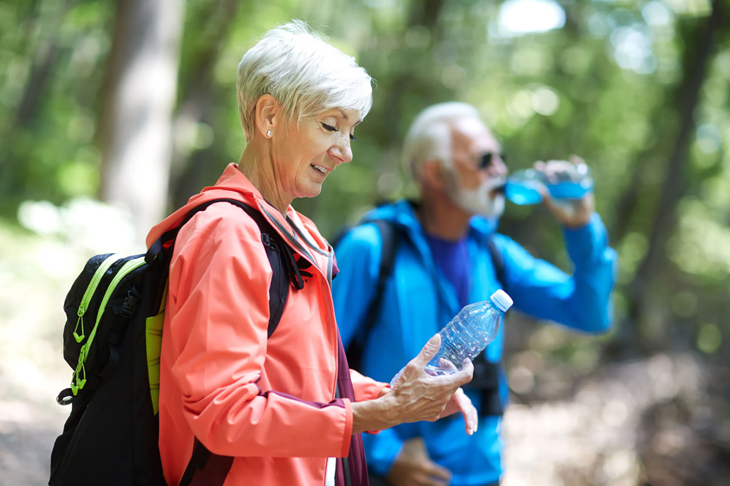 A man and woman out exploring nature each drink a bottle of water
