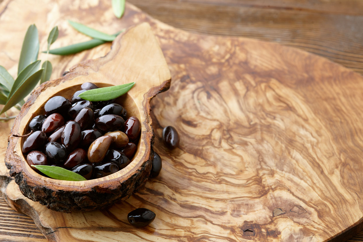 Fresh kalamata olives and olive tree leaves in an authentic greek wooden bowl