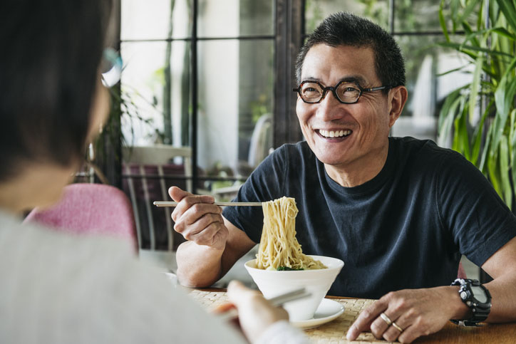 Mature man eating bowl of noodles and laughing