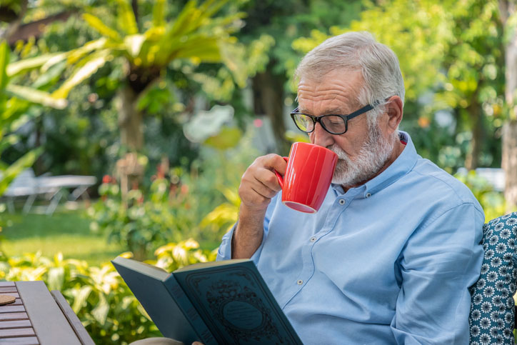 Man reading book while drinking from mug of coffee