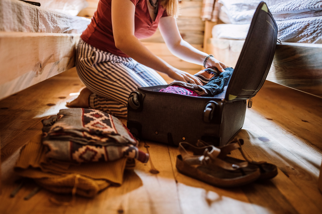 Woman packing luggage in log cabin, sitting on floor