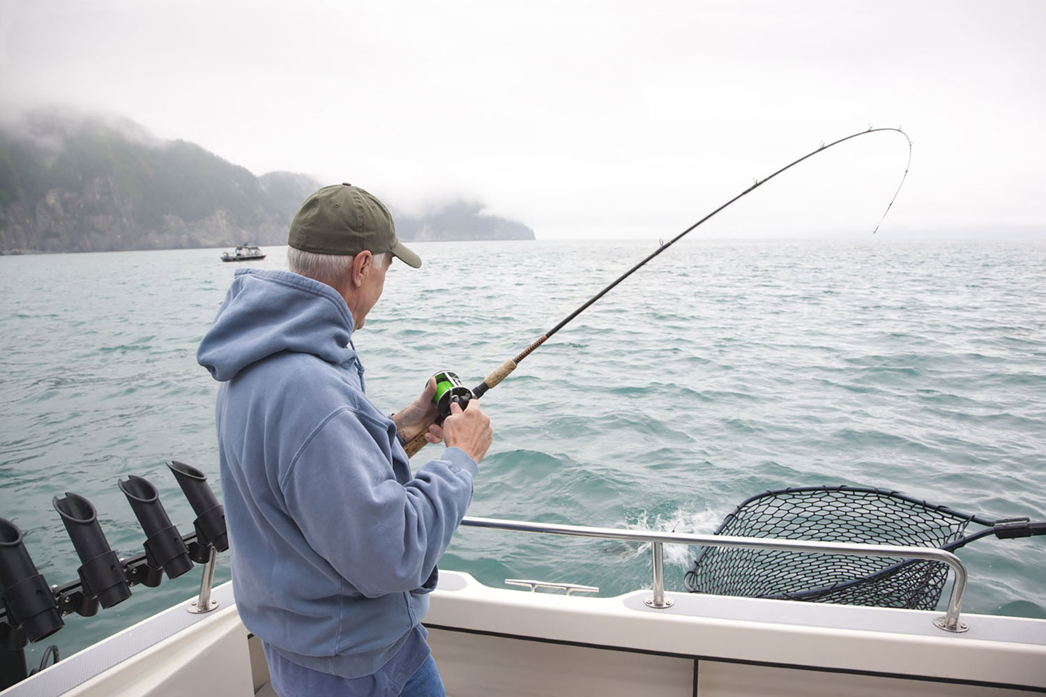 A senior man catches a salmon while fishing in Alaska