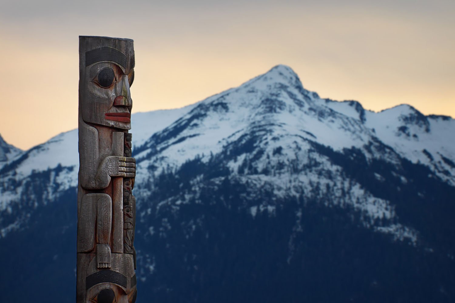 A totem pole looking towards and mountain in Alaska.