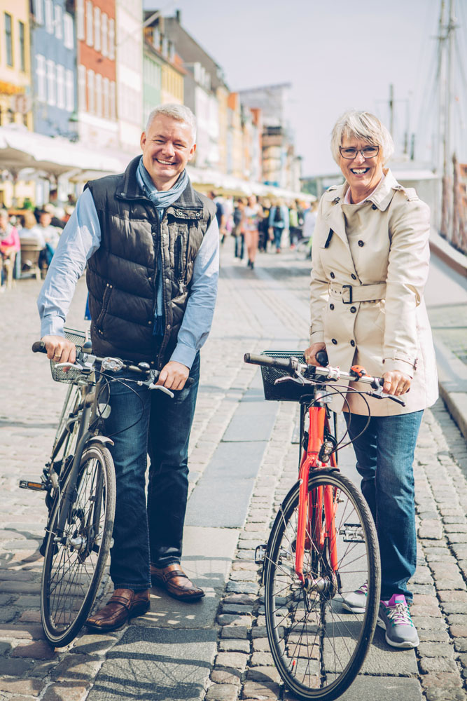 Mature couple poses while walking with bikes in Copenhagen.