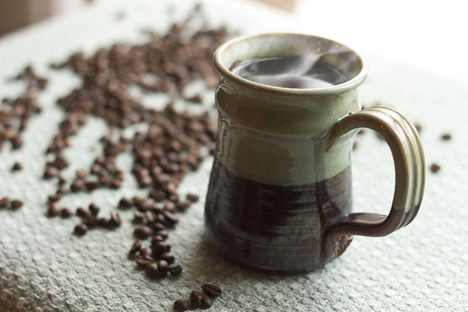 Steaming hot cup of morning coffee with coffee beans in background