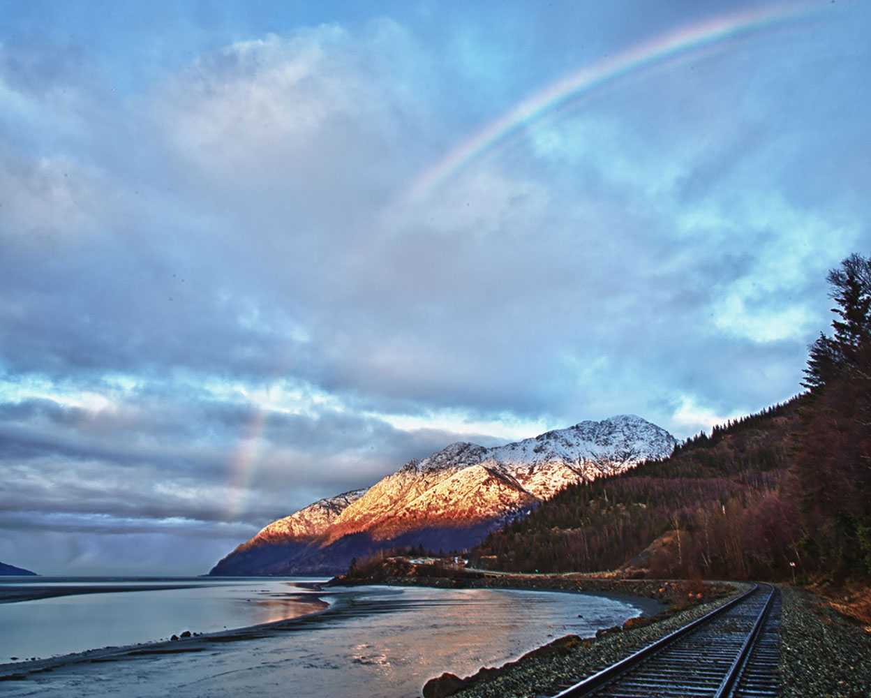 A rainbow stretches over a mountain range in Girdwood, Alaska.