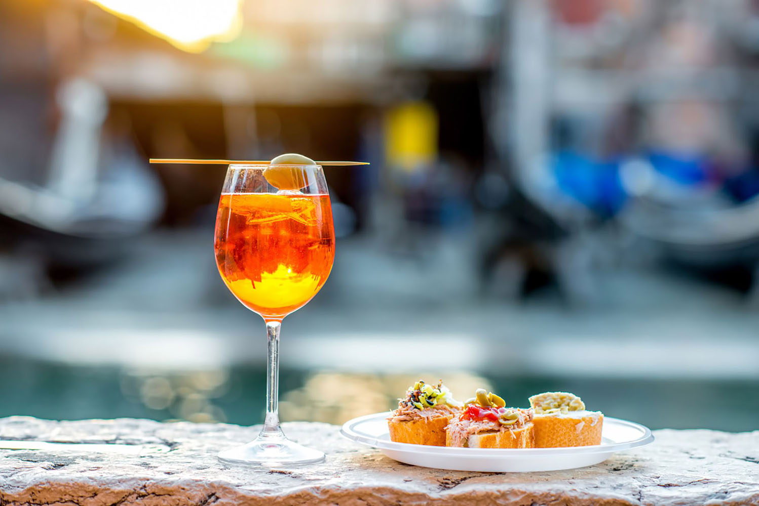 An Aperol Spritz cocktail is perched on a ledge in Venice, next to a plate of bruschetta.