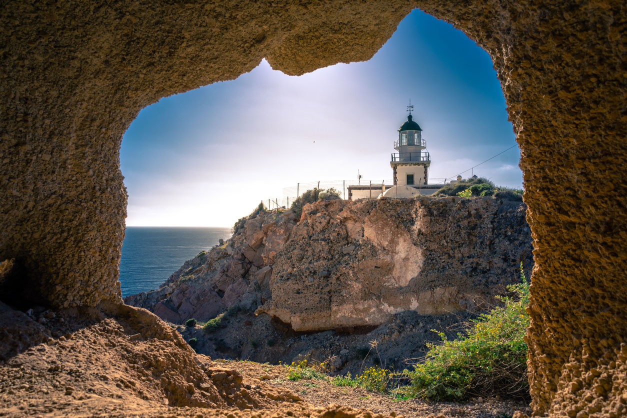 Lighthouse at Akrotiri through a frame of a window of a cave, Santorini, Greece