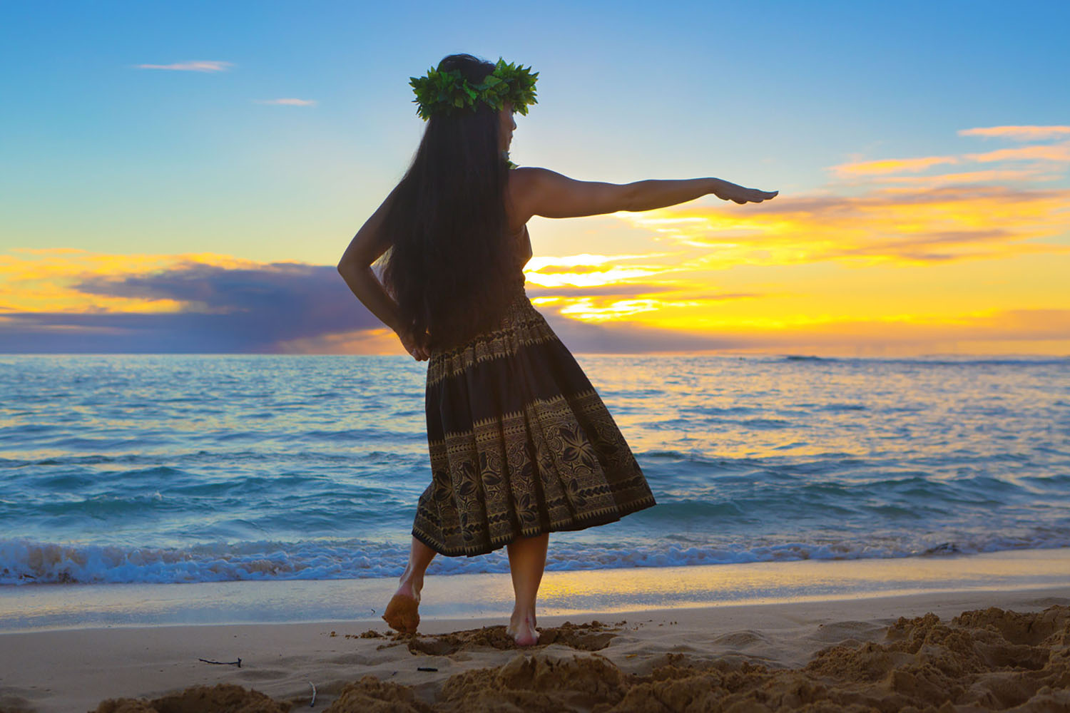 A Hawaiian woman dances in a luau as the sun sets beyond the beach