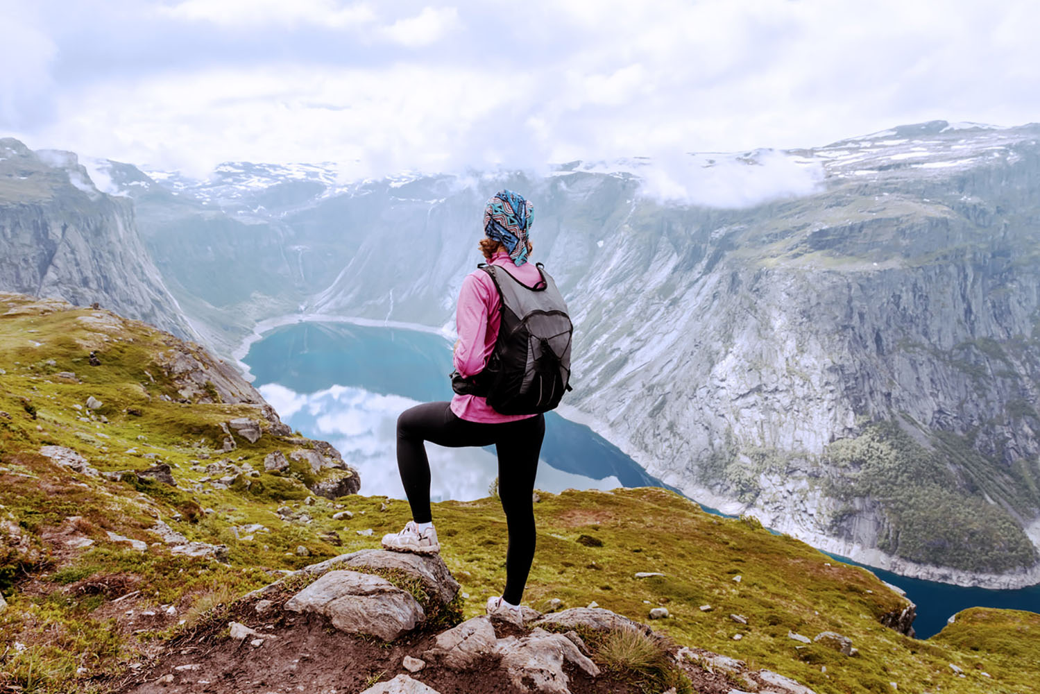 A woman dressed in athletic clothing looks out over a lake in the Norwegian Fjords.