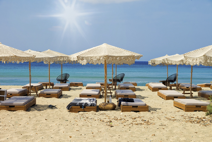 Umbrellas and Deck chairs on Agathopes Beach in Syros, Greece.