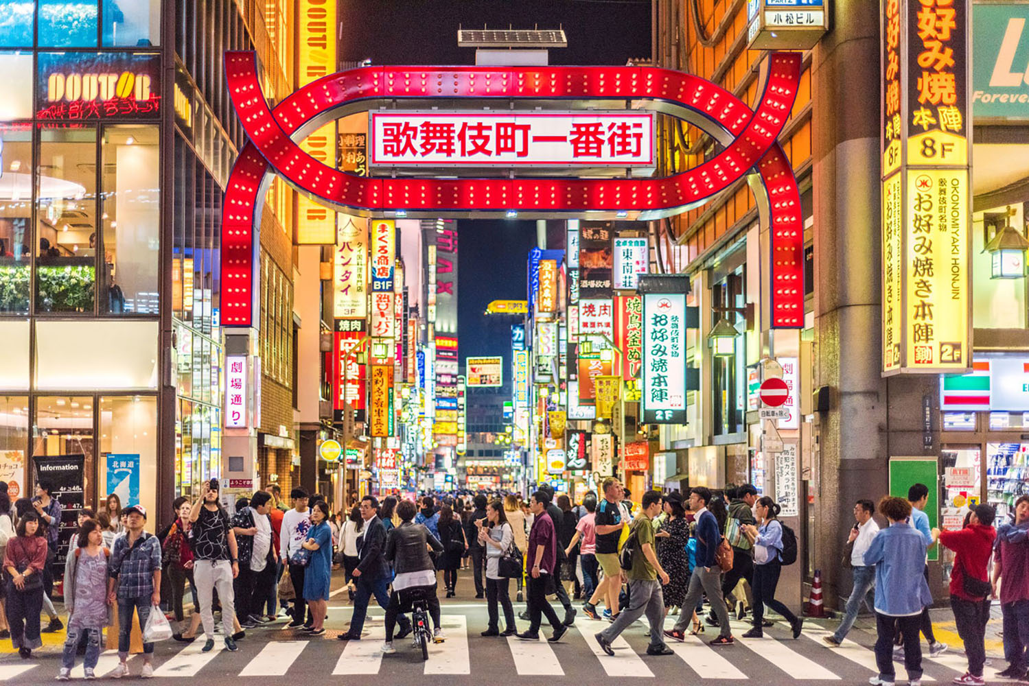 A large group of people walks through a bustling Japanese neighborhood