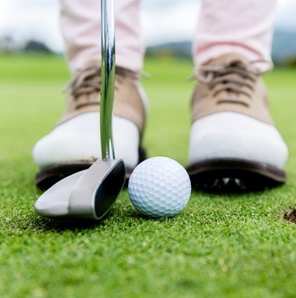person in golf shoes at hole with club and ball