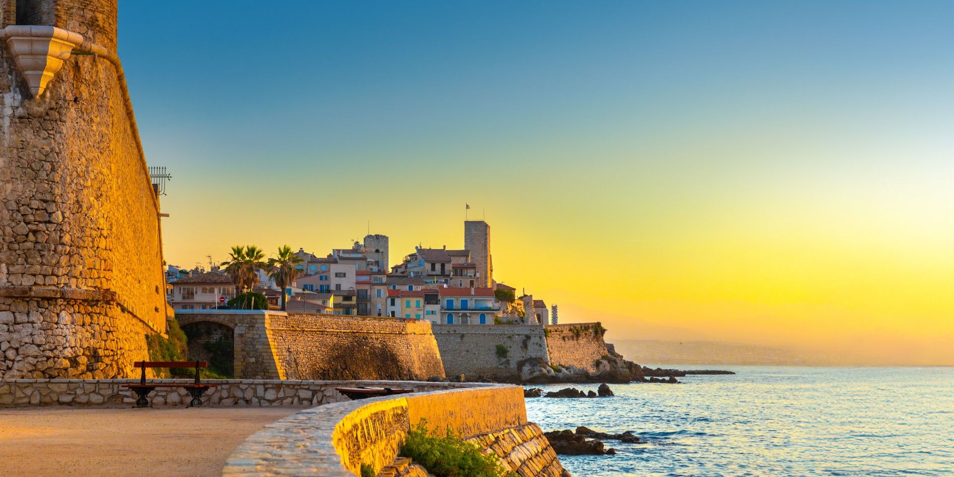 Sunlit view of Antibes’ historic stone walls and old town at sunset, overlooking the calm Mediterranean Sea.!'carousel'