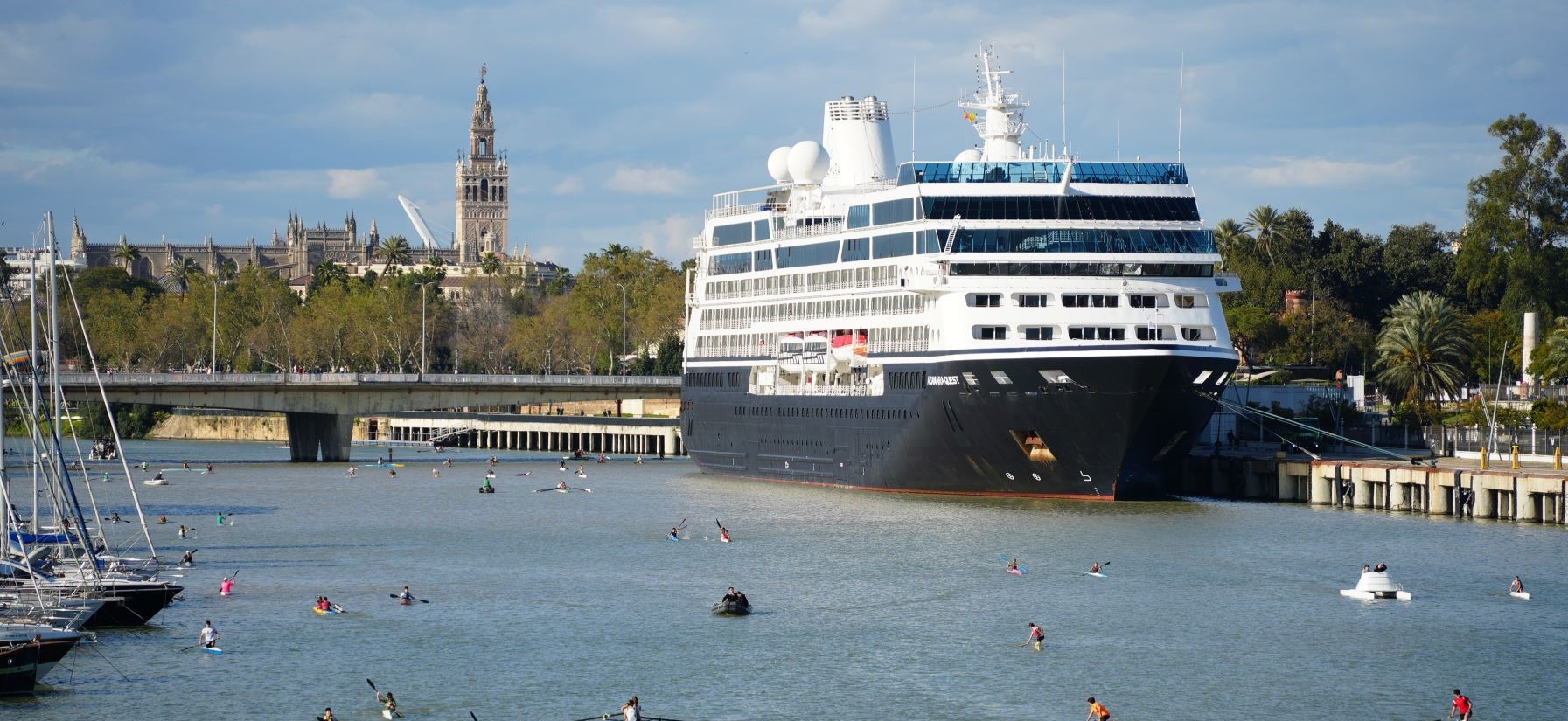 docked cruise ship in river behind kayakers in the water on a sunny day