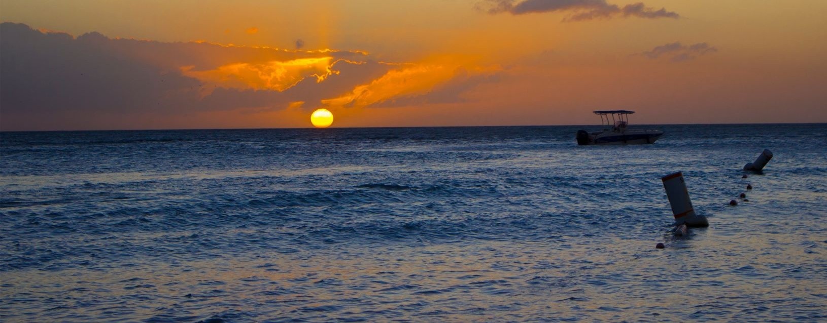 Sunset over open ocean with gentle waves and a distant boat.