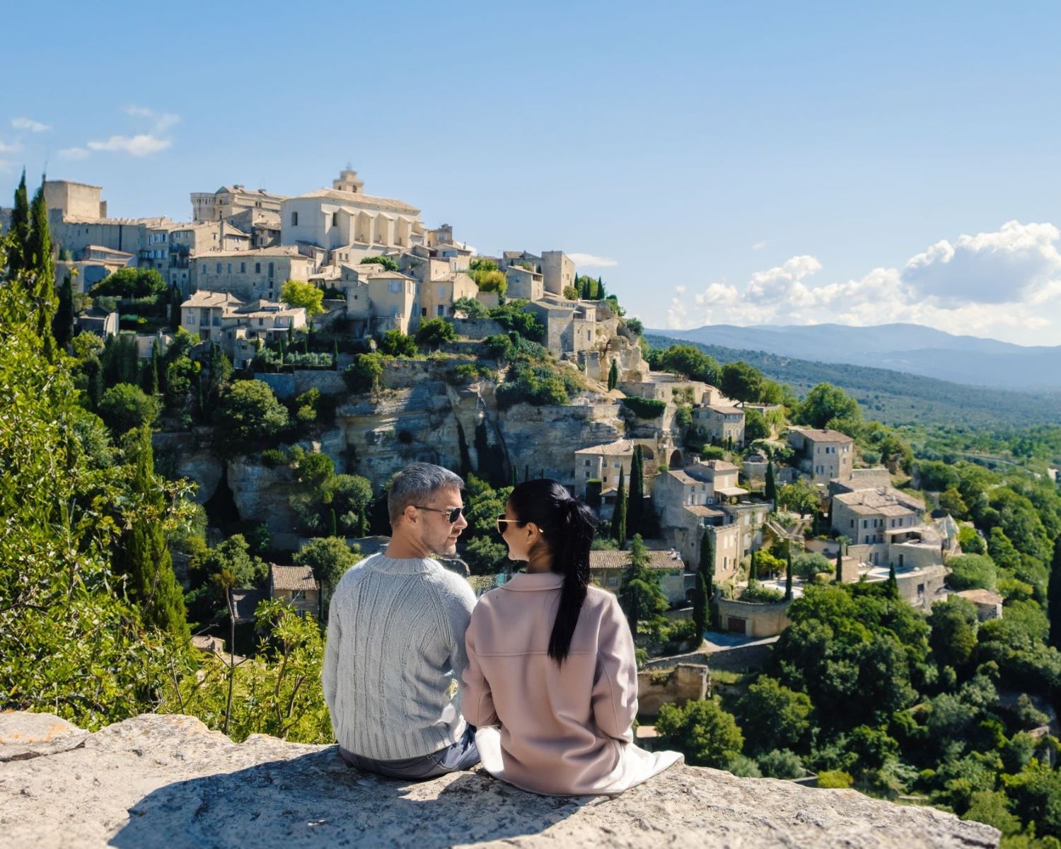 couple looking at each other sitting on cliff overlooking scenic view on a bright sunny day